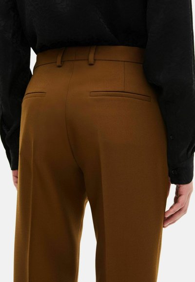 Bruine op maat gemaakte broek met een gladde textuur, voorzien van twee achterzakken en een aangesloten ontwerp. Gecombineerd met een zwart shirt met lange mouwen.