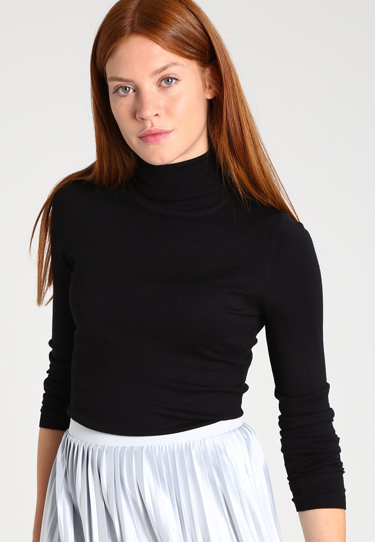 Schwarzer Rollkragenpullover aus dehnbarem Stoff, mit langen Ärmeln, figurbetonendem Design, kombiniert mit einem gefältelten, hellgrauen Rock.