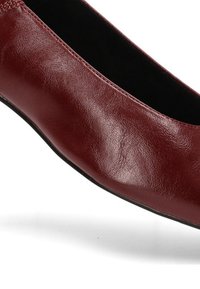 Bailarina de cuero burdeos con una textura suave, punta redondeada y costuras mínimas. Forro interior negro y suela flexible.