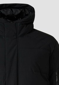 Schwarze Steppjacke mit hohem Kragen, glatter Außenseite, gesteppter Textur und minimalistischem Design. Verfügt über eine seitliche Reißverschlusstasche.