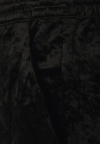 Tissu en velours noir à la texture douce, présentant un motif légèrement froissé et des coutures visibles, disposé en plis lâches.