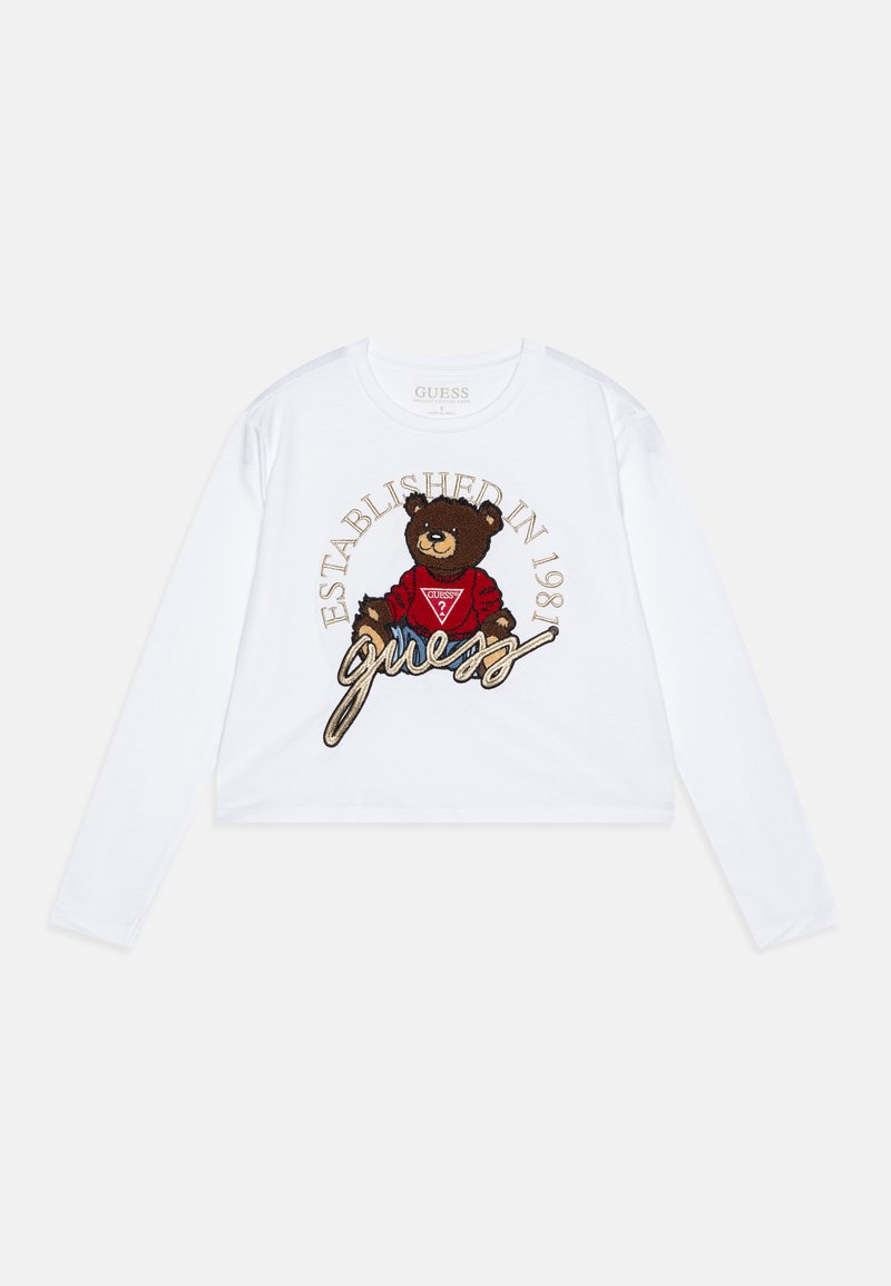Cropped top blanco de manga larga con un gráfico de un oso marrón que lleva una camiseta roja con el texto "GUESS" y "ESTABLECIDO EN 1981" bordado en dorado.