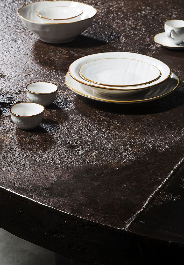 Weißes Keramikteller-Set mit goldener Umrandung, einschließlich Schalen und Tellern, auf einer dunklen strukturierten Oberfläche angeordnet.