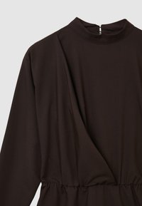 Dunkelbraunes Langarmkleid mit Stehkragen, gerafftem Taillenbereich und überlappendem Vorderteil auf einem schlichten hellen Hintergrund.