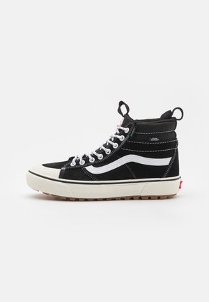 Baskets montantes noires avec accents blancs, en suède et toile, semelle en caoutchouc, couture contrastante et deux languettes au niveau de la cheville.