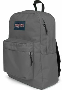 Sac à dos Jansport gris avec une poche avant, fabriqué en tissu durable. Il possède des fermetures éclair et une poignée à boucle sur le dessus pour un transport facile.