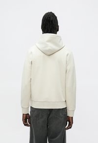 Κρεμ φούτερ με απαλό ύφασμα, με μεγάλη κουκούλα και ριμπ μανσέτες, συνδυασμένο με σκούρο γκρι τζιν άνετης γραμμής.