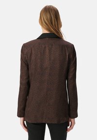 Blazer con stampa animalier marrone, dotato di colletto nero, spalle strutturate e vestibilità sartoriale, realizzato in un tessuto liscio e leggero.