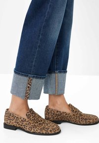Dunkelblaue Jean mit Leopardenmuster-Trimm, kombiniert mit tanfarbenen und schwarzen Leopardenmuster-Pantoletten auf nackten Füßen.
