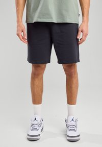 Black athletic shorts with a smooth fabric, drawstring waist, and side pockets, paired with white sneakers and crew-length socks.