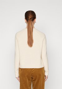 Hellbeige Pullover mit weicher Textur, rundem Ausschnitt und geripptem Saum, kombiniert mit Cordhosen in einem warmen Braunton.
