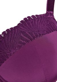 Violetinio liemenėlė su tekstūriniu nėriniuotu paviršiumi ir banguotu kraštu, o apačioje – lygus audinys. Reguliuojamos petnešėlės užbaigia dizainą.