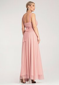 Długa różowa sukienka z dopasowanym gorsetem i szerokimi ramiączkami, z kokardą na plecach i lejącą się spódnicą z przezroczystą nakładką.