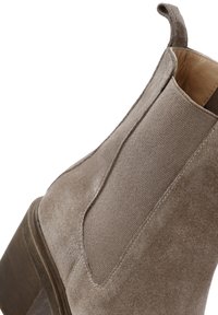 Stivaletto in camoscio di colore marrone chiaro con pannelli laterali elasticizzati, punta rotonda e tacco in legno. Dettaglio di cucitura evidente sul camoscio.