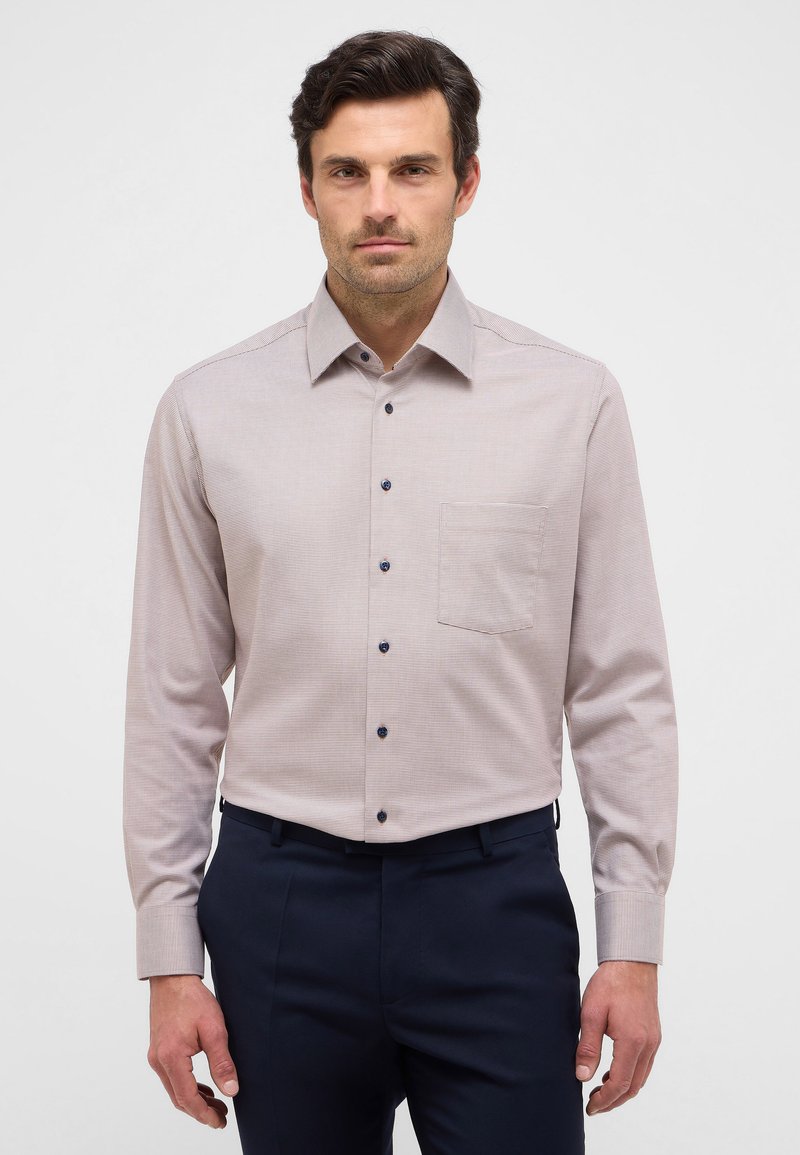 Camicia a maniche lunghe a quadri color marrone chiaro con colletto button-down, dotata di bottoni blu e taschino sul petto, abbinata a pantaloni scuri.