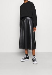 Maglietta nera a maniche lunghe abbinata a una gonna midi in pelle nera lucida e sneakers alte nere con lacci bianchi e logo.