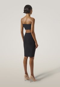 Svart axelbandslös klänning med en figursydd silhuett, knälång, som matchas med nude högklackade skor. Slät tygkänsla och minimalistisk design.
