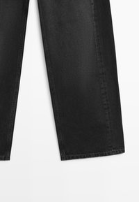 Pantaloni in denim nero con taglio dritto, caratterizzati da sfumature discrete, linee pulite e cuciture a contrasto lungo le cuciture esterne.
