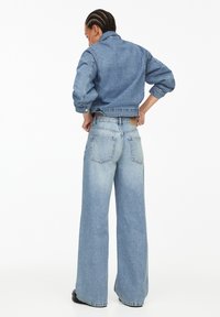 Denim jack met brede broekspijpen in lichtblauw. De jack heeft een kraag en elastische manchetten; de broek heeft achterzakken en een leren label.