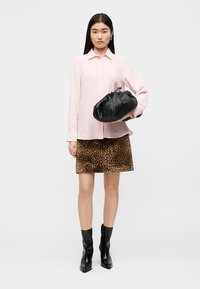 Ροζ πουκάμισο με κουμπιά, φούστα με λεοπάρ σχέδιο, μαύρη τσάντα με υφή και μαύρες ψηλοτάκουνες μπότες μέχρι το γόνατο σε μοντέλο μπροστά από ουδέτερο φόντο.