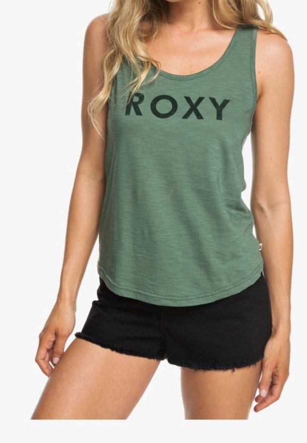Camiseta sin mangas verde con escote redondo, con un gran texto negro "ROXY". Combinada con pantalones cortos de mezclilla negros y deshilachados. Diseño ligero y casual.