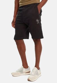 Pantaloni neri corti in misto cotone, con vita elasticizzata e tasche laterali. Include un dettaglio del logo ricamato bianco sulla coscia.