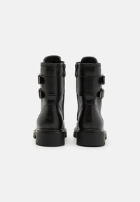 Botas de tobillo de cuero negro con un diseño elegante, dos hebillas decorativas en el lateral y un tacón robusto para mayor estabilidad.