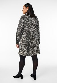 Vestido de leopardo con mangas largas, cuello redondo y silueta recta. Tela en tonos de gris y negro, combinado con zapatos negros.