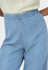 Pantalones de tiro alto en azul claro, confeccionados en una suave tela texturizada. Cuentan con una cinturilla lisa y piernas holgadas para mayor comodidad.