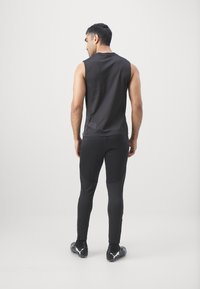 Zwarte mouwloze sporttop gecombineerd met zwarte, strakke broek. De outfit heeft een gladde textuur, een minimaal ontwerp en contrasterend zwart schoeisel.