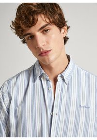 Chemise légère à boutons avec des rayures verticales bleues et vertes, base blanche, et un logo brodé sur la poitrine. Design classique à col.