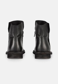 Bottines en cuir noir avec une finition lisse, une forme légèrement fuselée et un talon empilable. Dotées d'une fermeture éclair sur le côté pour un enfilage facile.