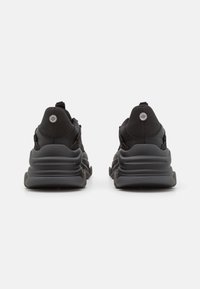 Chaussures de sport noires avec tige en mesh, col rembourré, amorti proéminent au talon et logo circulaire sur le talon.