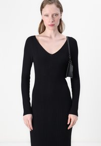 Long-sleeve, black ribbed dress with a V-neckline. The fabric is stretchy, fitted along the body, and features a subtle vertical texture.