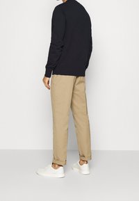 Felpa navy con colletto tondo, pantaloni beige a gamba stretta e sneakers bianche. Outfit casual, mostrato di spalle su uno sfondo neutro.