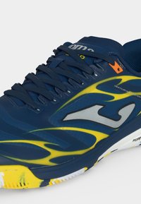 Αθλητικό παπούτσι ναυτικού μπλε με κίτρινο σχέδιο φλόγας, γκρίζο λογότυπο, μαύρα κορδόνια και σύστημα αερισμού σε λευκή σόλα.