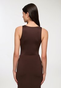 Brązowa dopasowana sukienka bez rękawów, o gładkiej fakturze i wysokim dekolcie. Tył ma czysty szew i przylegający do ciała krój.