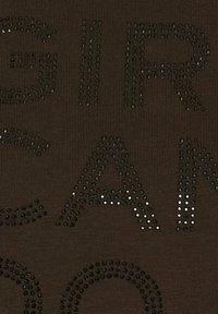 Brunt stof med en ribbet tekstur, prydet med store sorte rhinsten, der danner bogstaver. Designet fremhæver en dristig, grafisk stil.