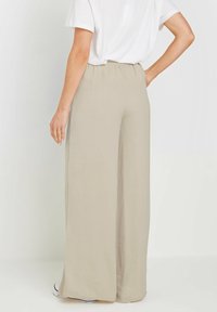 Light beige wide-leg trousers with an elastic waistband, made from a smooth fabric, featuring a flowing design and minimal crease texture.
