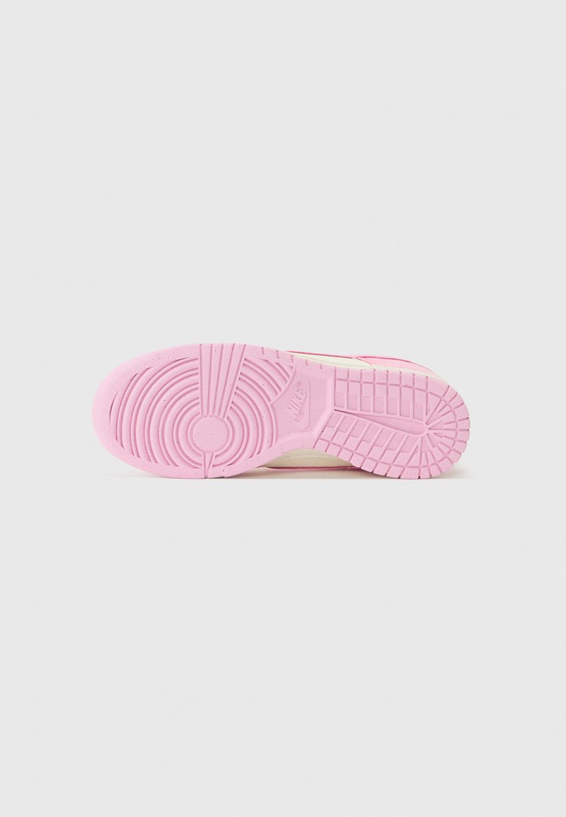 Baskets Nike avec une semelle en caoutchouc, principalement roses, ornées de motifs circulaires et en chevron, texture lisse et accents minimaux.