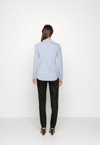 Light blue long-sleeve shirt with a pointed collar, paired with black tailored trousers and heeled sandals, shown from behind.