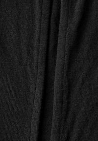 Mustan neulotun kankaan hieno rakenne, jossa on hienovaraiset urat ja pehmeä pinta, aseteltuna taitteisiin kerroksellisen ilmeen luomiseksi.