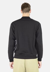 Černá mikina s dlouhými rukávy, žebrovanými manžetami a zadní pohled ukazující bílé akcenty podél boků. Měkk�á struktura látky.