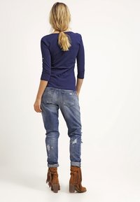 Marinblå långärmad topp, ljusblå slitna jeans och bruna fransiga ankelstövlar. För en avslappnad look är jeansen något uppvikta vid fållarna.