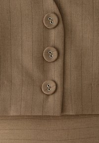 Bruine stof met dunne verticale strepen, met drie bijpassende ronde knopen die elk met twee gaten verticaal op een rij zijn genaaid.