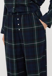 Housut, joissa on ruudullinen flanellikangas syvänsinisessä, vihreässä ja valkoisessa. Vatsaa myötäilevä elastinen vyötärö, sivutaskut ja nappikoristeet. Pehmeä rakenne.