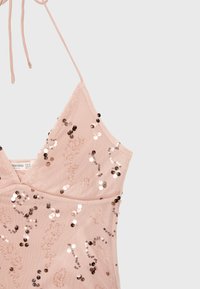 Robe rose clair à fines bretelles avec des sequins dispersés en motifs floraux sur un tissu transparent.