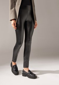 Leggings de imitación cuero negros con una cintura alta, con un acabado brillante. Combinados con mocasines negros de suela texturizada.