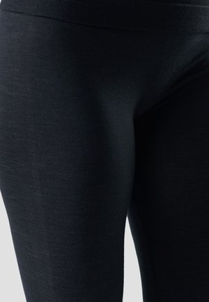 Close-up van zwarte leggingstof en naden op het bovenbeen tegen een neutrale achtergrond.