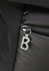 Kotna torba iz črnega blaga z gladkim, sijočim zadrgo, ki ima kovinski povodnik s poudarjenim črko "B". Teksturiran neoprenski material.